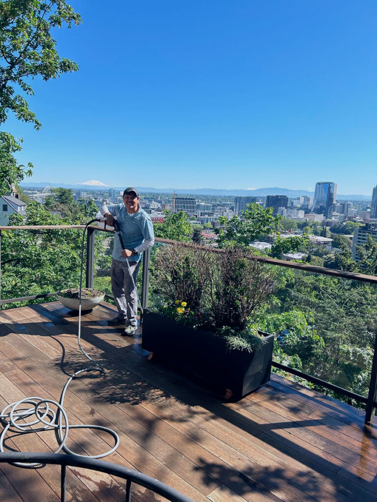 Dou-Glass team member performing pressure washing on elevated deck with panoramic Portland city and Mount Hood view in Oregon – reliable and professional service